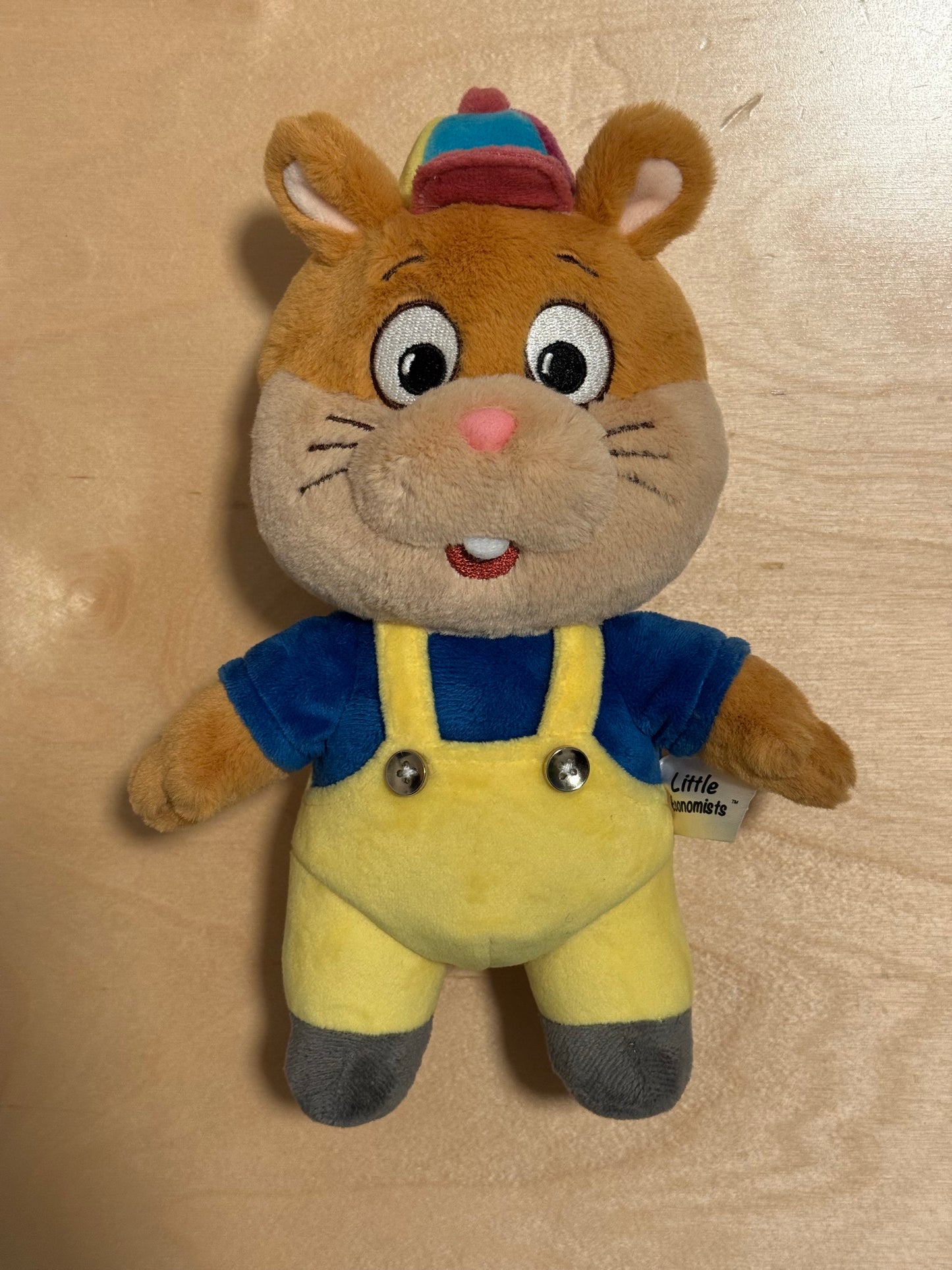 Plush toy resembling a hamster in a blue outfit on a beige background