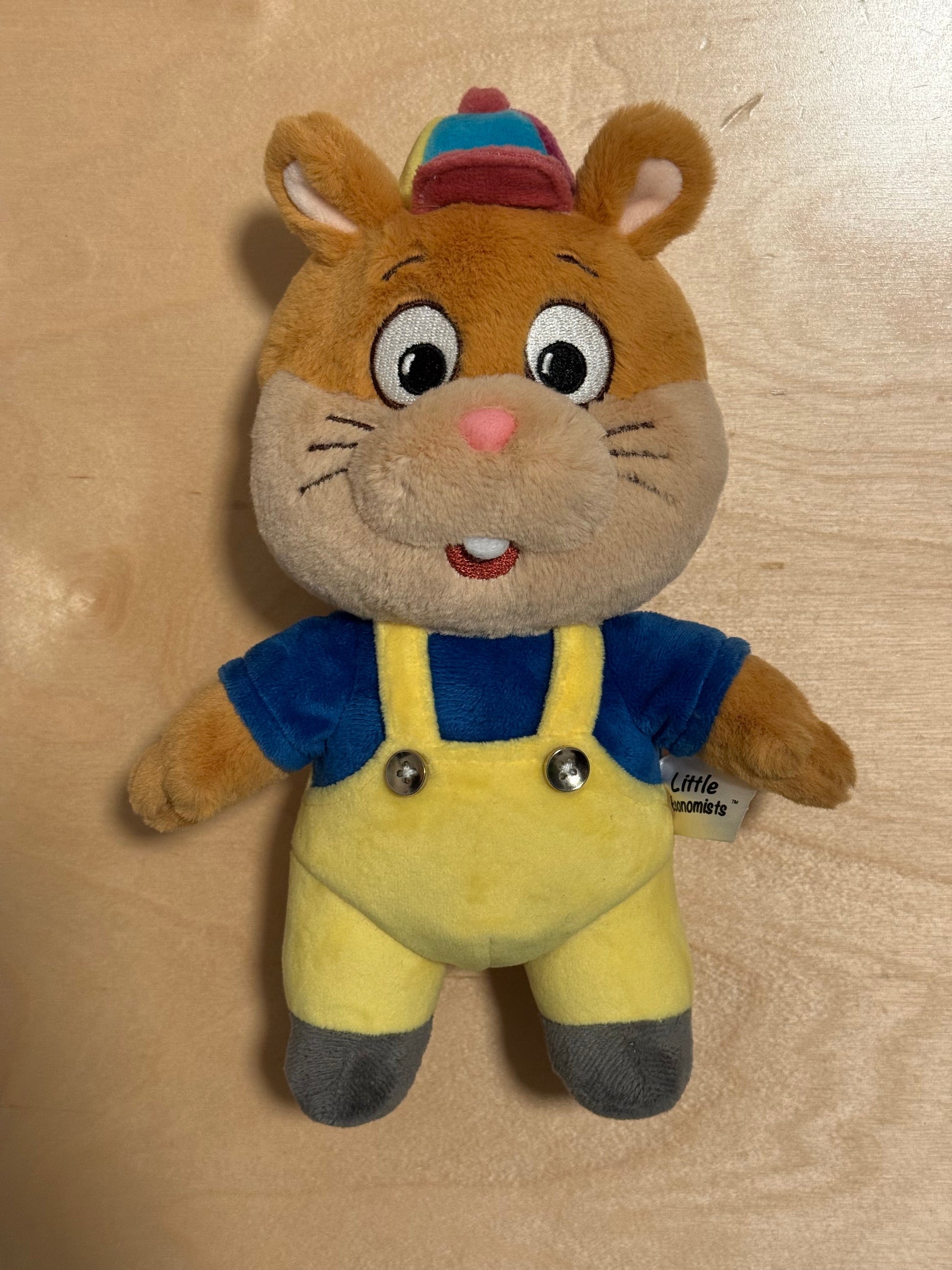 Plush toy resembling a hamster in a blue outfit on a beige background